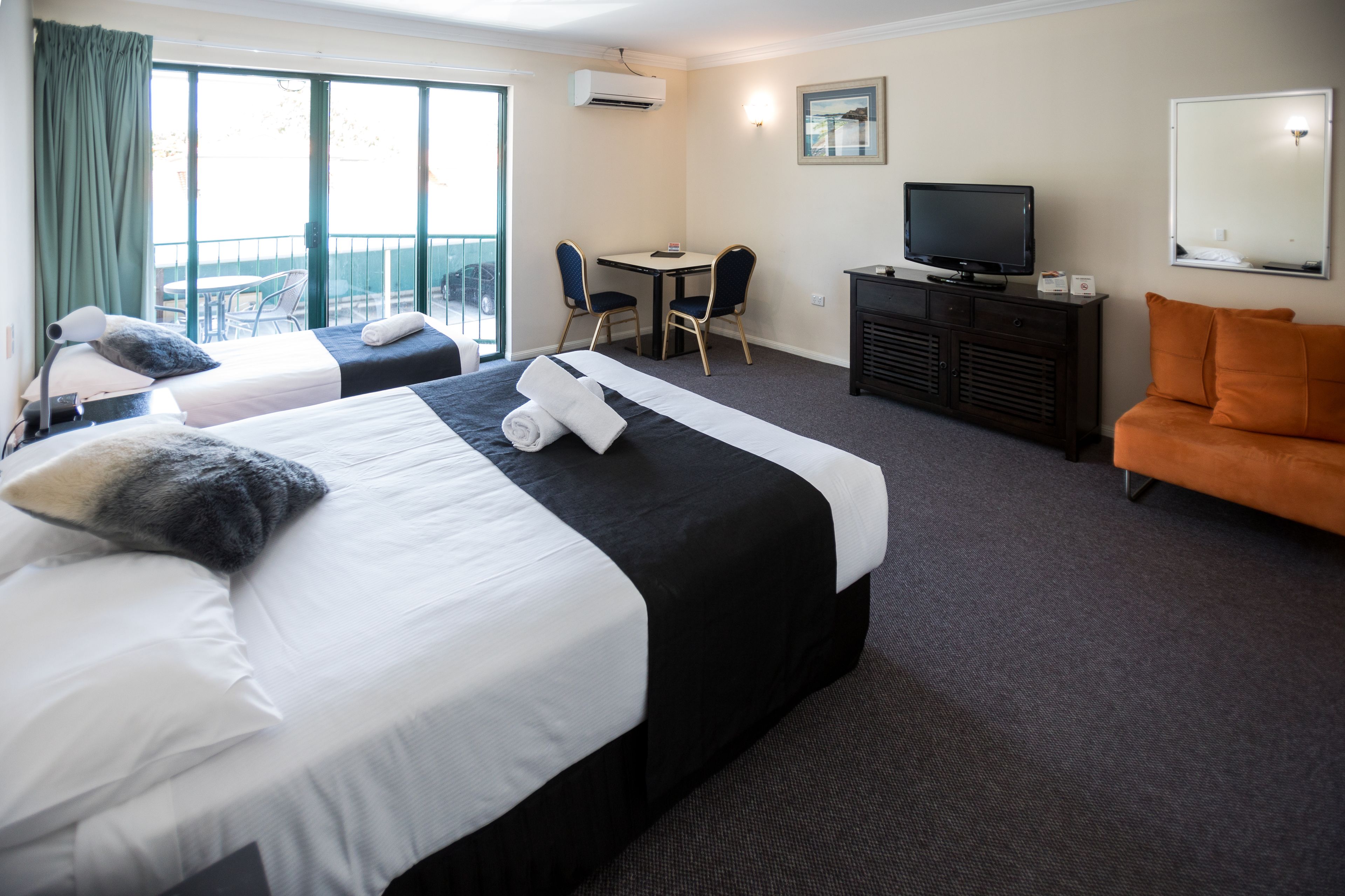 A hotel room with two beds, a desk with chairs, a television, and a sofa.