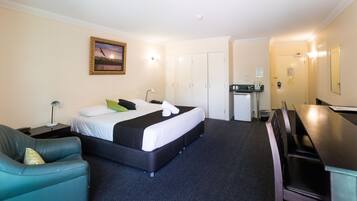 Quarto de hotel com cama, escrivaninha, cadeira, armário e cozinha compacta.