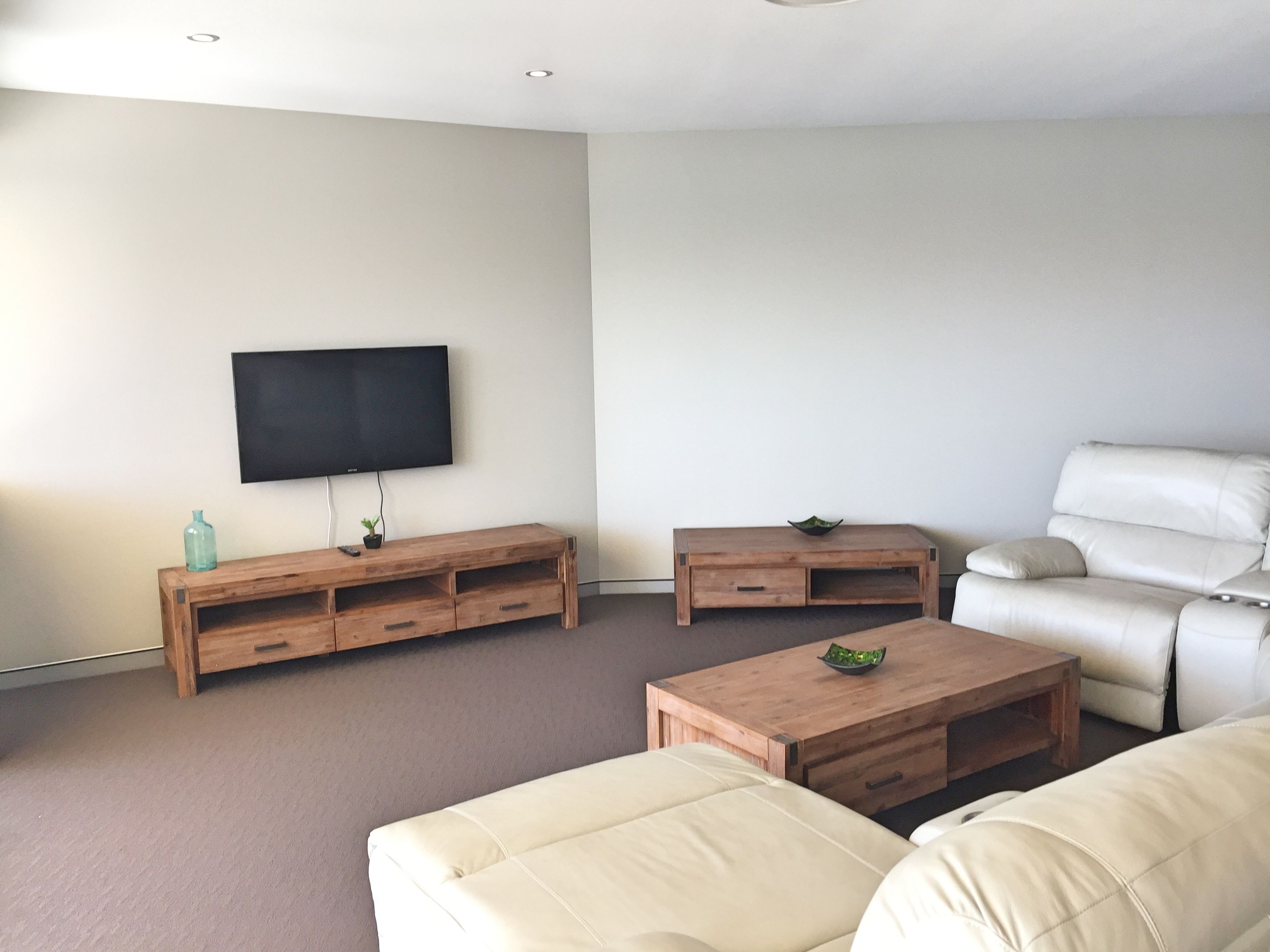 A living room with a flat-screen TV, wooden entertainment unit, beige sofa, and a small coffee table.