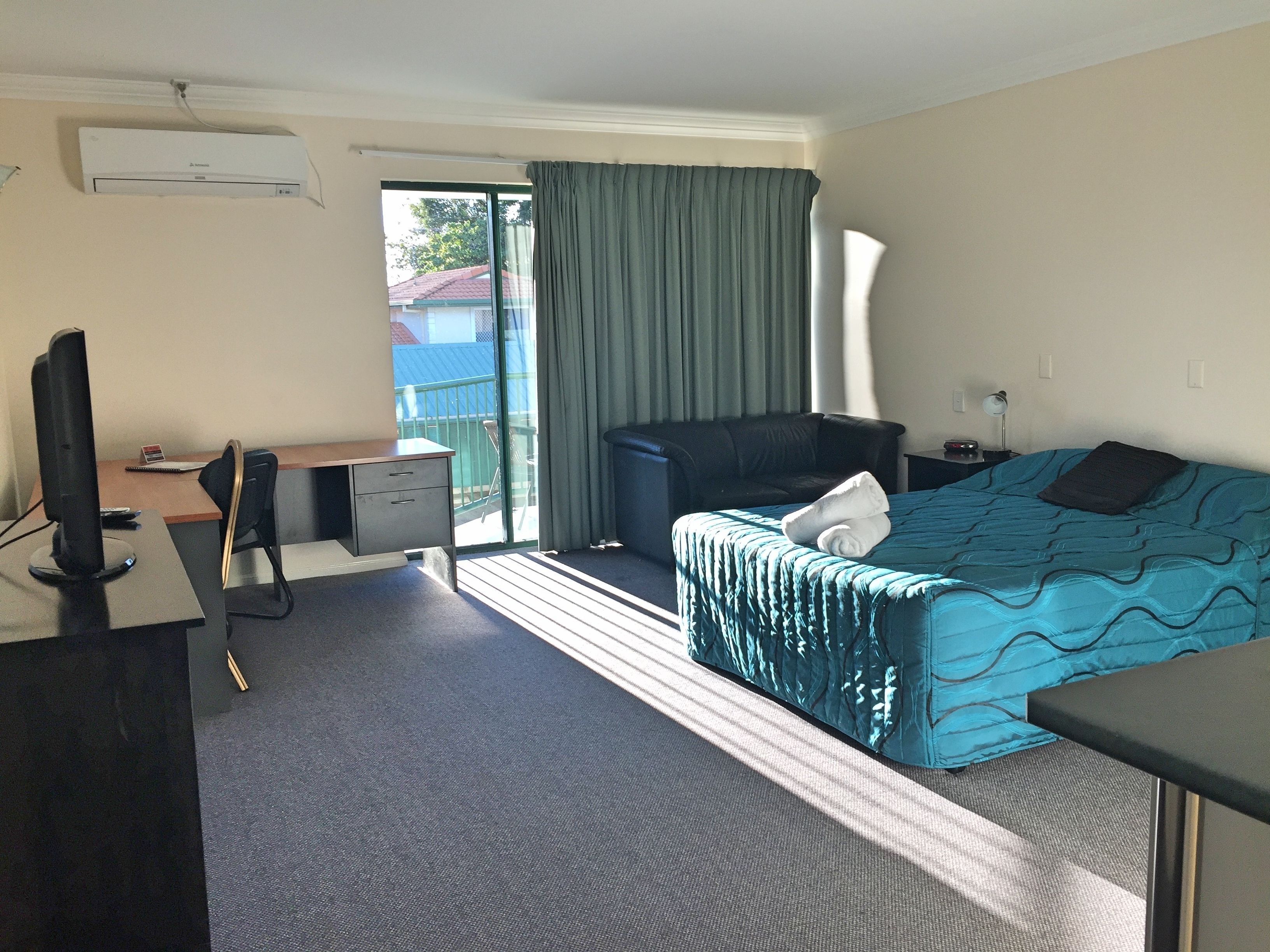 A hotel room with a bed, a desk with a computer, a chair, a TV, and a window with curtains.