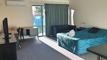 A hotel room with a bed, a desk with a computer, a chair, a TV, and a window with curtains.