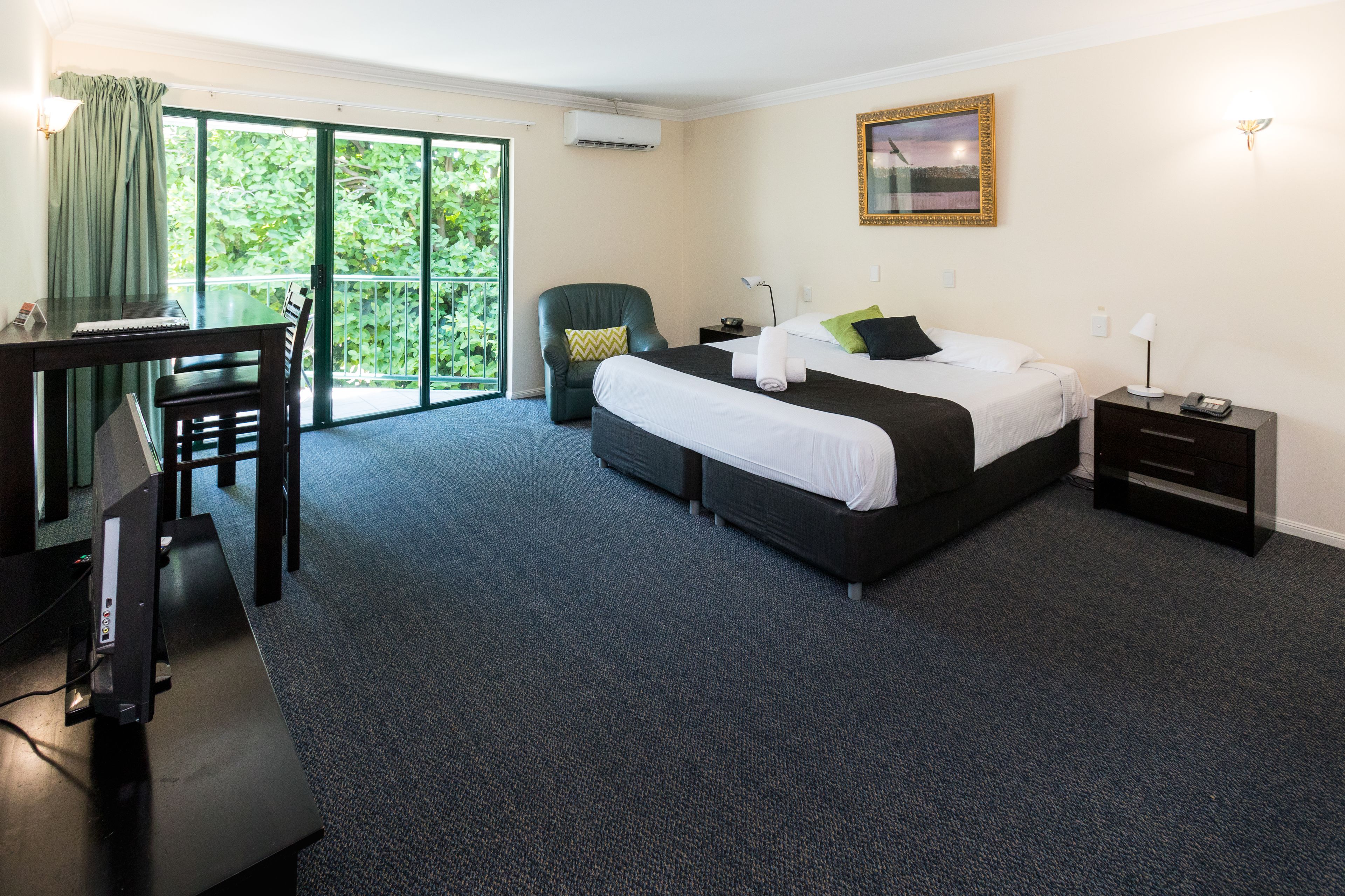 Une chambre d’hôtel avec un grand lit, un bureau, une chaise, une petite table et un balcon donnant sur un paysage verdoyant.