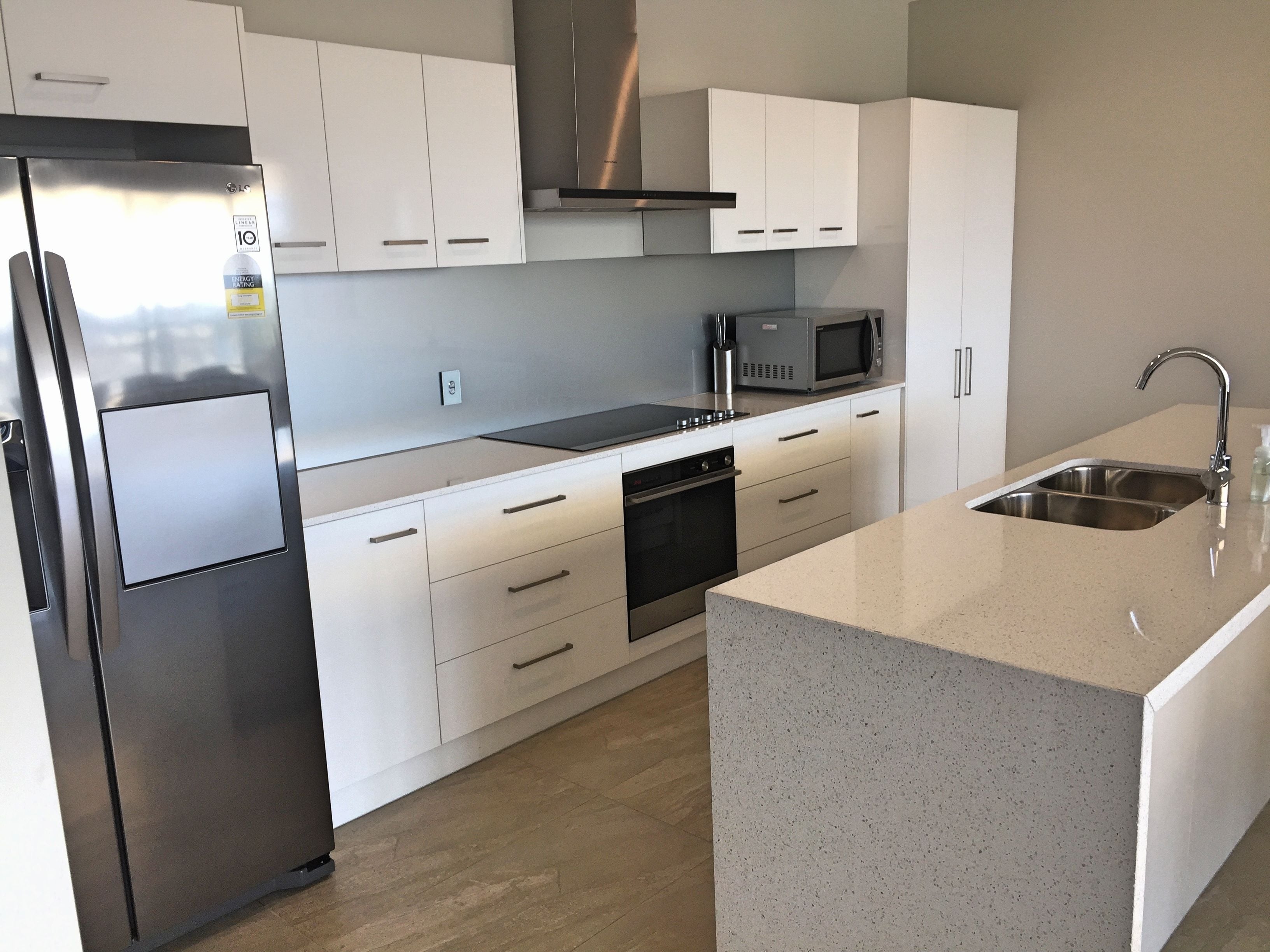 A modern kitchen with white cabinets, stainless steel appliances, a microwave, and a sink.