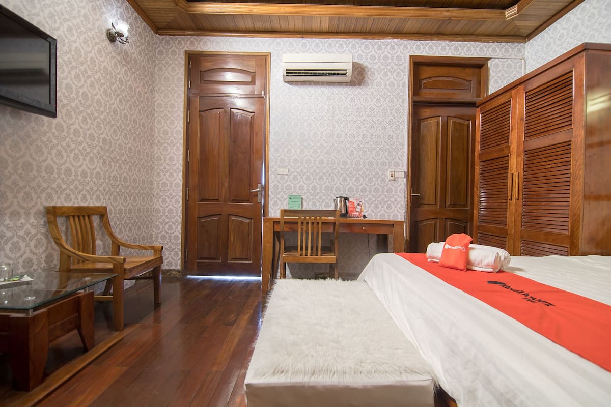 Habitación de hotel con un escritorio de madera, una silla, una cama con cubrecama blanco y una toalla roja.
