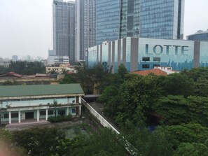A building with a sign reading "LOTTE" in the background, surrounded by greenery and other buildings. - Green Hotel (Hanoi)