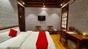 A hotel room with a bed, a desk, two chairs, a television, and a window with stained glass. - Green Hotel (Hanoi)