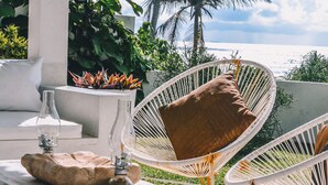 A hammock chair with a brown cushion, a stone planter, and a glass bottle on a terrace with a view of the ocean and palm trees. - W15 Escape (Ahangama)
