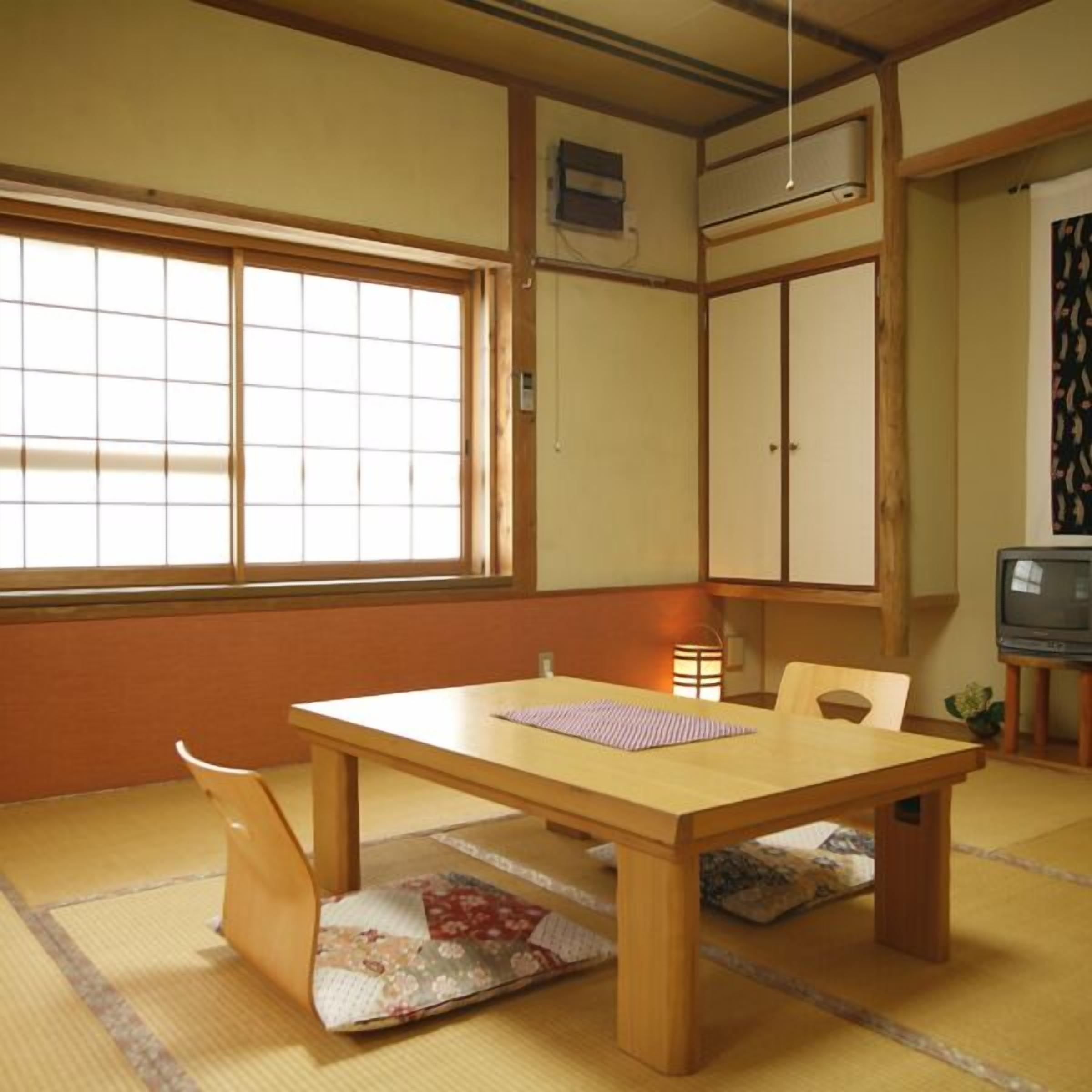 A traditional Japanese room with tatami flooring, a low wooden table, a television, and sliding doors.