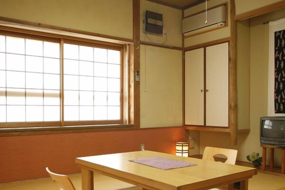 A traditional Japanese room with tatami flooring, a low wooden table, a television, and sliding doors.
