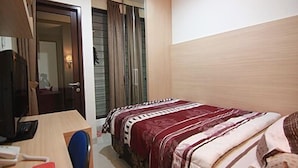 Una habitación de hotel con cama, escritorio con silla, televisión y armario.