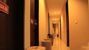 Un pasillo de hotel con un letrero que dice 'IDAK ADA' a la izquierda, barriles de madera a lo largo de la pared y una escalera a la derecha.