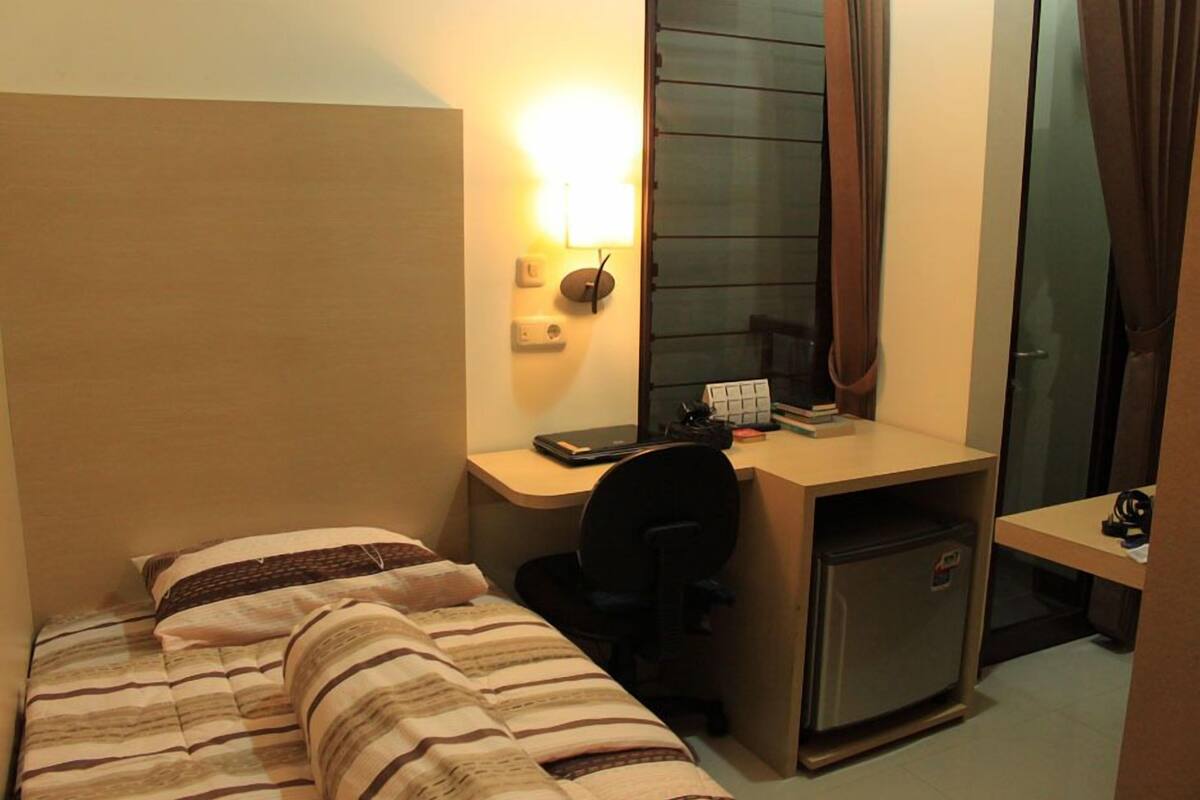 A compact hotel room with a single bed, a desk with a computer, and a small refrigerator.