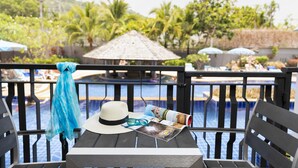 A poolside table with a hat, sunglasses, and a magazine, overlooking a pool with umbrellas and palm trees. - Pgs Hotels Casa Del Sol (Kata)