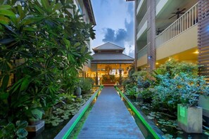 A pathway leading to a building with a traditional roof, surrounded by lush greenery and a water feature. - Pgs Hotels Casa Del Sol (Kata)
