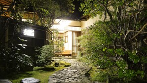 A stone pathway leading to a traditional Japanese building at night, surrounded by lush greenery and rocks. - Hashinoya Annex Ransui (Kobe)