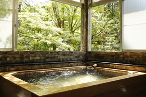 A hot tub with a view of a lush garden through a window. - Hashinoya Annex Ransui (Kobe)