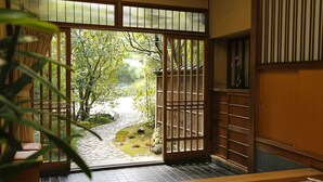 A traditional Japanese room with tatami flooring, a shoji screen door, and a view of a garden with a stone path. - Hashinoya Annex Ransui (Kobe)