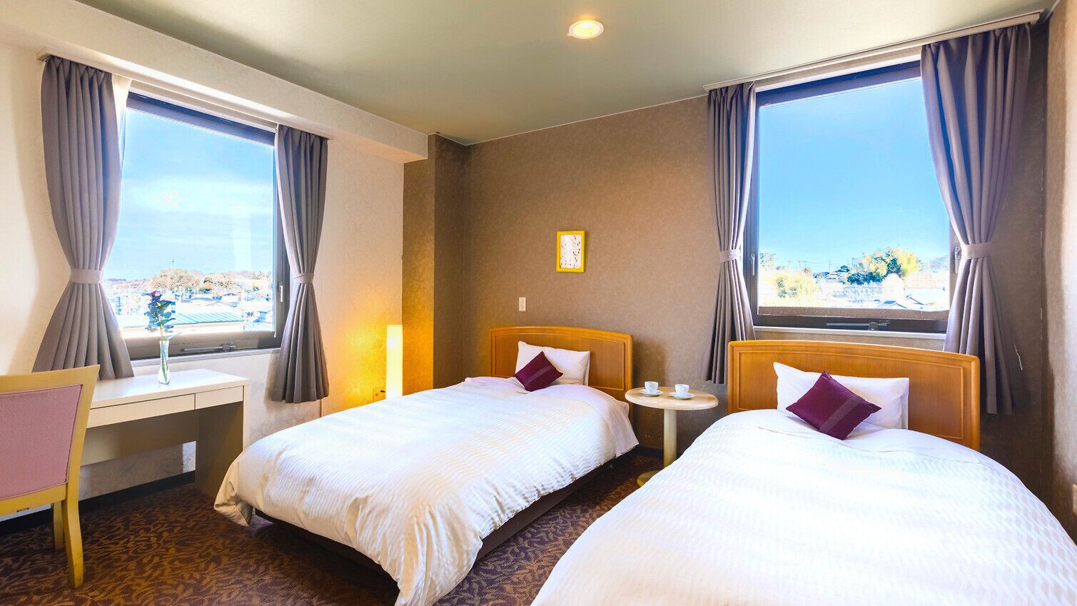 Hotelkamer met twee bedden, een bureau, een stoel, een tafeltje en uitzicht op een stadsbeeld.