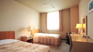 Habitación de hotel con dos camas, un escritorio con silla, teléfono y ventana con cortinas.