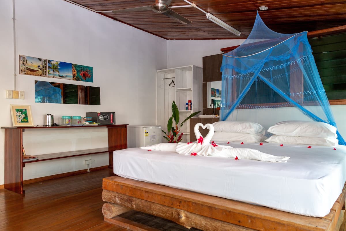 A neatly made bed with a canopy, a wooden bench, a small table with items, and a wall with framed pictures.