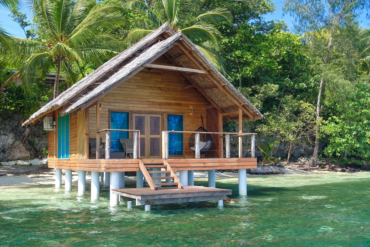 A wooden bungalow with a thatched roof, a balcony, and a small deck.