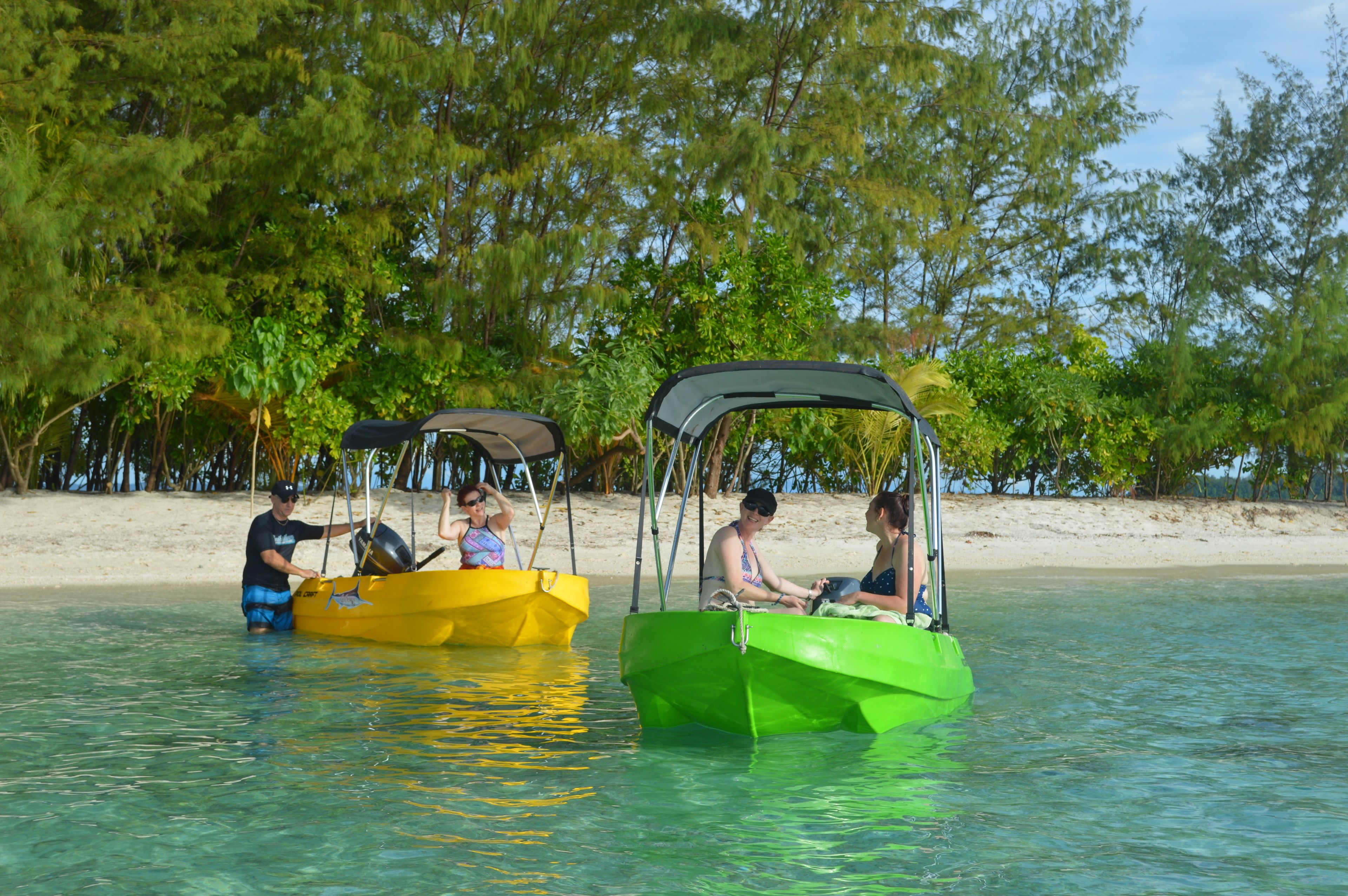 Dois barcos pequenos em águas calmas, com uma praia de areia e árvores densas ao fundo.