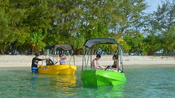 Dois barcos pequenos em águas calmas, com uma praia de areia e árvores densas ao fundo.