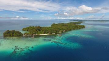 An aerial view of a tropical island with clear turquoise waters, lush greenery, and several small buildings.