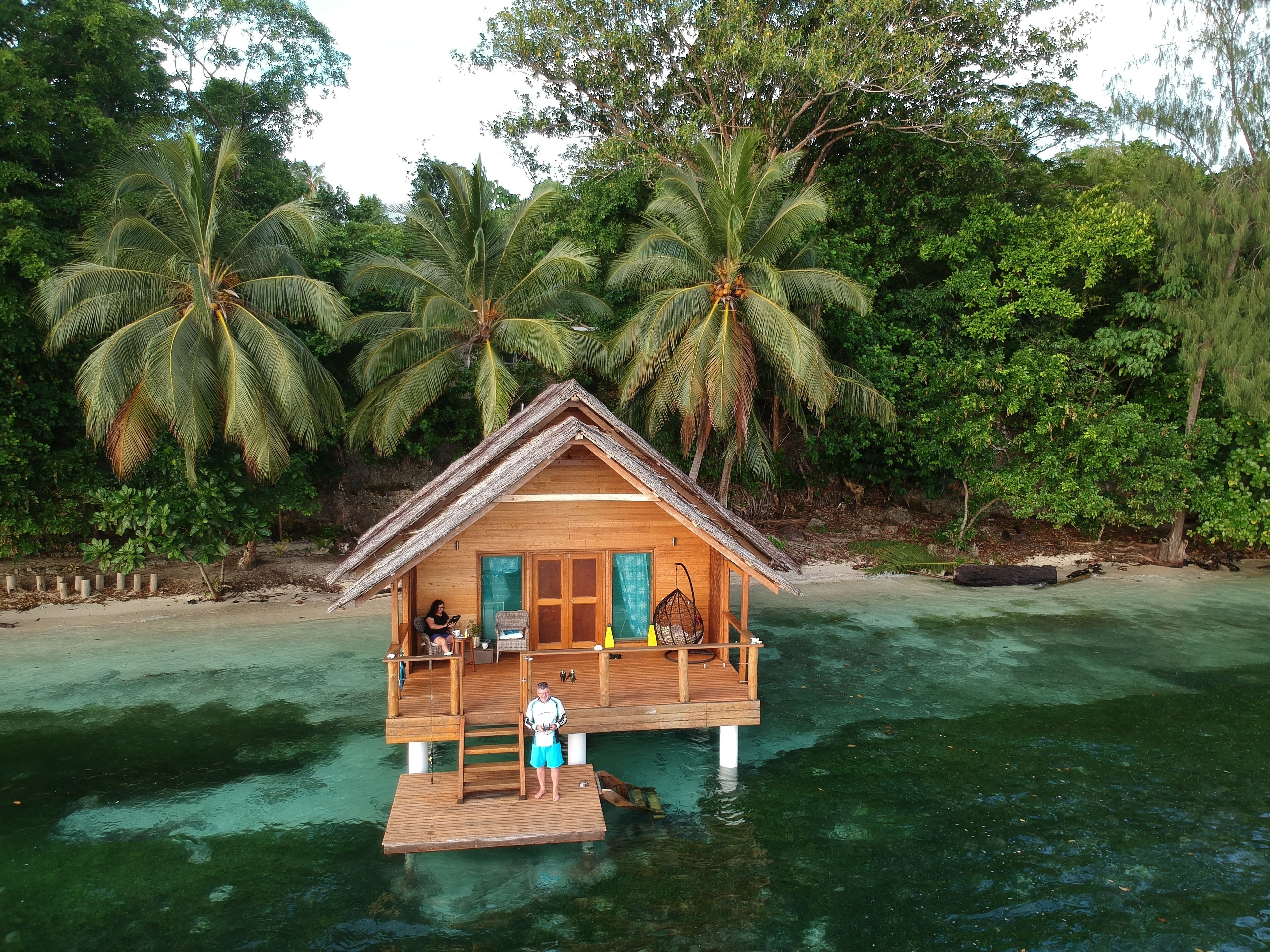 Een houten huis op palen boven helder water, omringd door palmbomen.