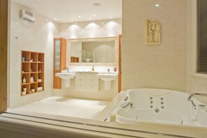 Une salle de bain moderne avec une grande baignoire, deux lavabos, un meuble-lavabo avec un miroir et une étagère contenant des articles de toilette.