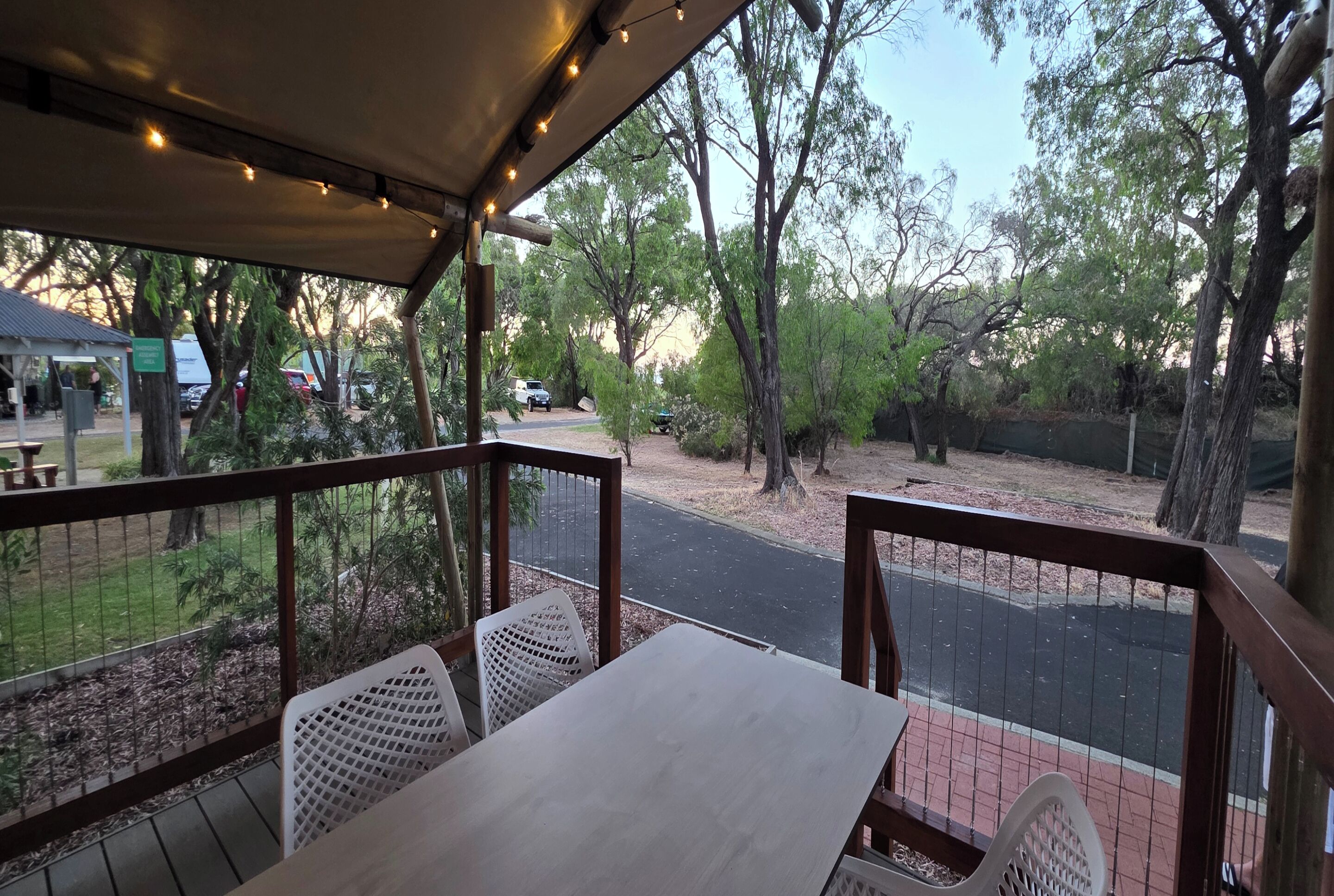 Een overdekt terras met tafels en stoelen, met uitzicht op een weg en bomen.