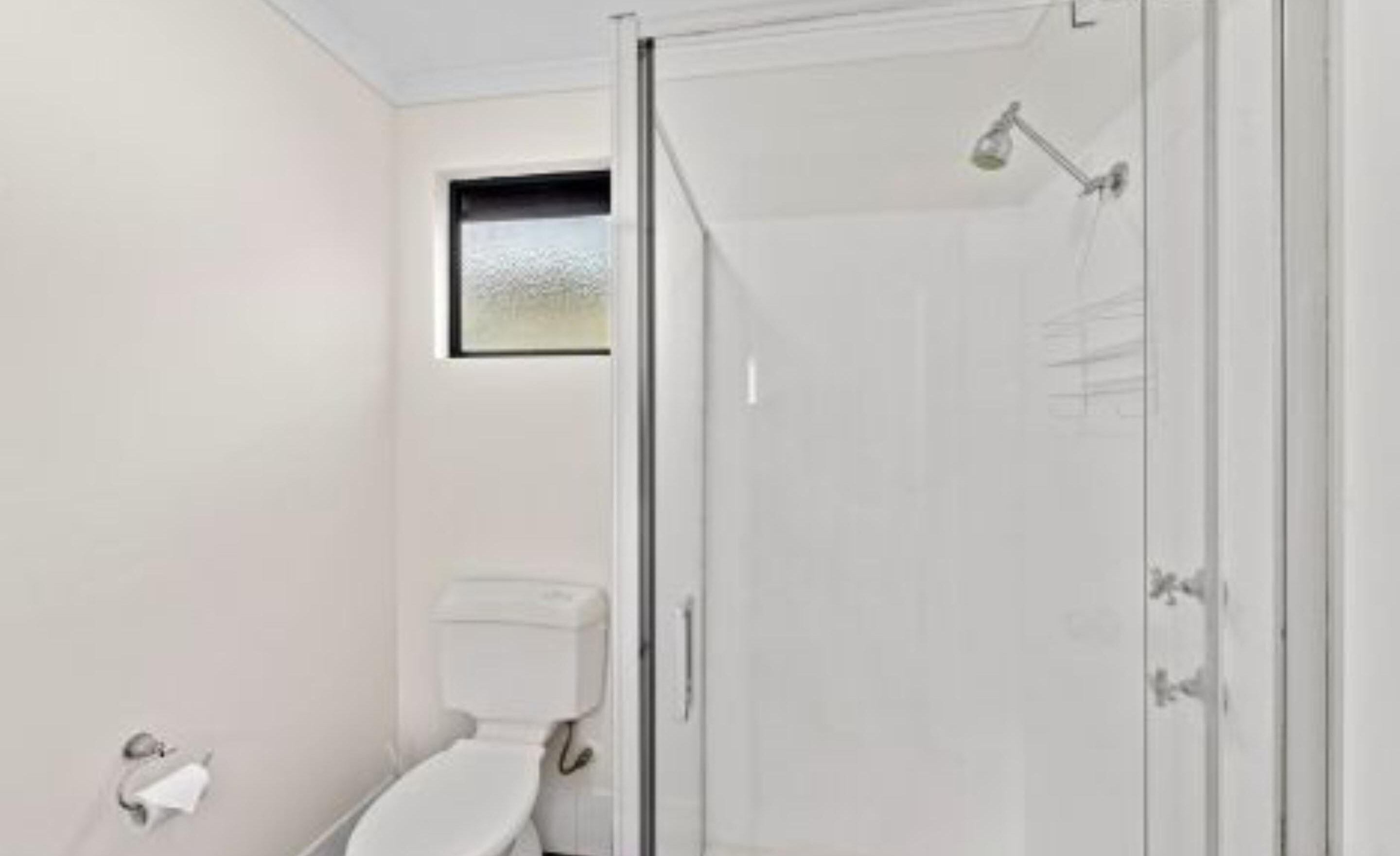 Un baño moderno con inodoro, cabina de ducha y una ventana pequeña.