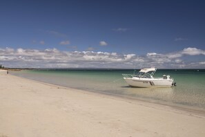 Un bote en una playa arenosa con agua cristalina y un cielo parcialmente nublado.
