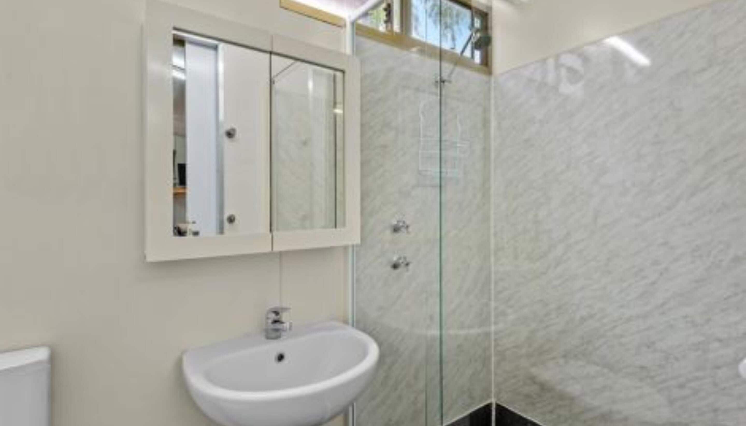 Un baño con lavamanos blanco, cabina de ducha de vidrio y espejo sobre el lavamanos.