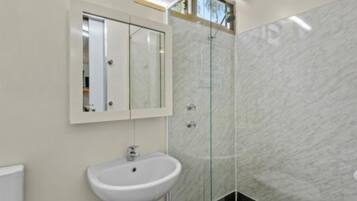 Un baño con lavamanos blanco, cabina de ducha de vidrio y espejo sobre el lavamanos.