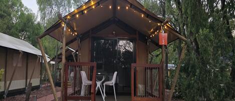 A small, wooden cabin with a porch and two white chairs, surrounded by trees.