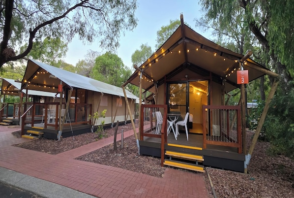 A small, wooden cabin-style structure with a porch and string lights, surrounded by trees.