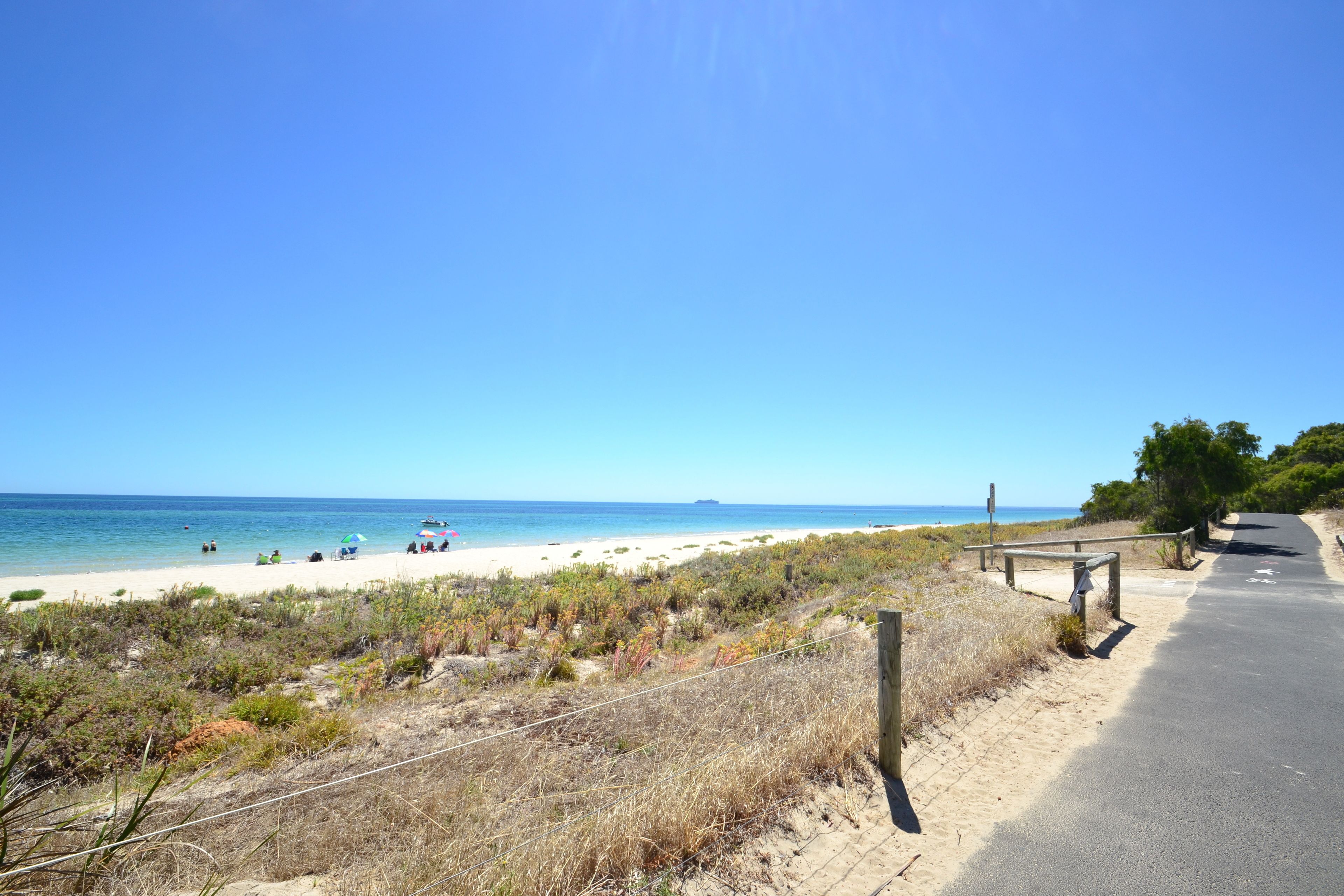 A beach with a paved path, sandy dunes, and the ocean in the background.