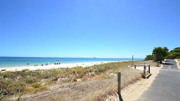 A beach with a paved path, sandy dunes, and the ocean in the background.