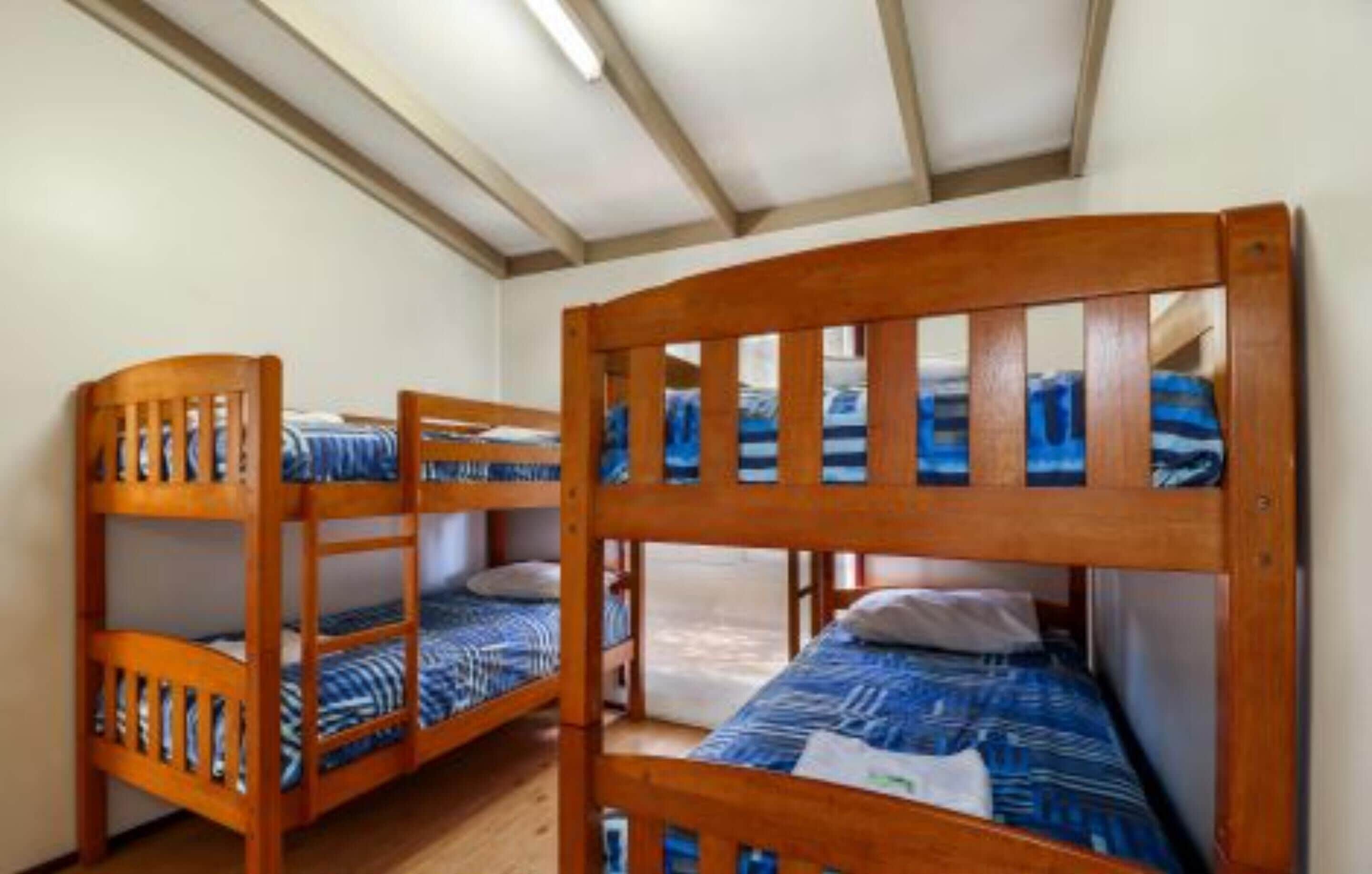 Una habitación con tres literas, cabeceros de madera y techo inclinado con vigas a la vista.