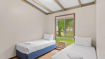 A room with two beds, a small table, and a window with a view of greenery.