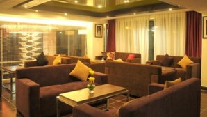 A modern hotel room with a seating area featuring sofas and armchairs, a coffee table, and a large window with curtains.