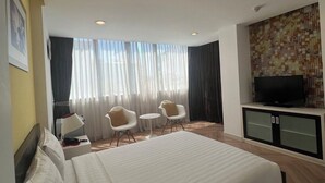 A hotel room with a large bed, two chairs, a small table, a TV, and a wall with a mosaic pattern.