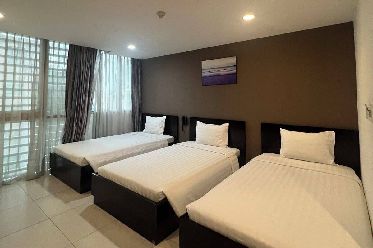 Habitación de hotel con tres camas, un ventanal con cortinas y un cuadro en la pared.