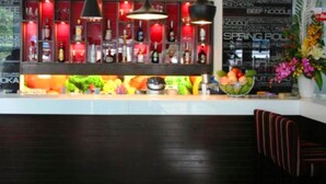 A bar area with a counter, hanging pendant lights, and a variety of bottles and fruits displayed.