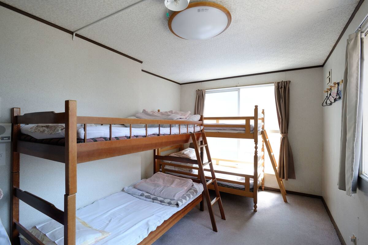 A bunk bed room with a ladder, a window with curtains, and a ceiling light fixture.