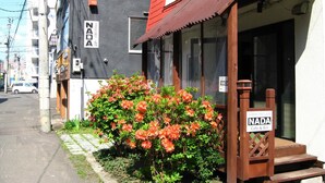 A building with a 'NADA' sign, a small garden with orange flowers, and a wooden structure labeled 'Sapporo Inn Cafe & Bar'. - Sapporo Inn NADA - Hostel (Sapporo)