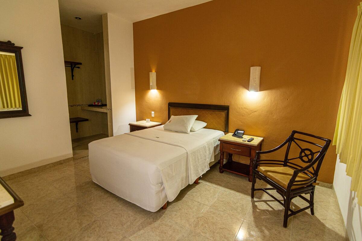 A hotel room with a large bed, bedside tables, a chair, and a bathroom visible through an open door.