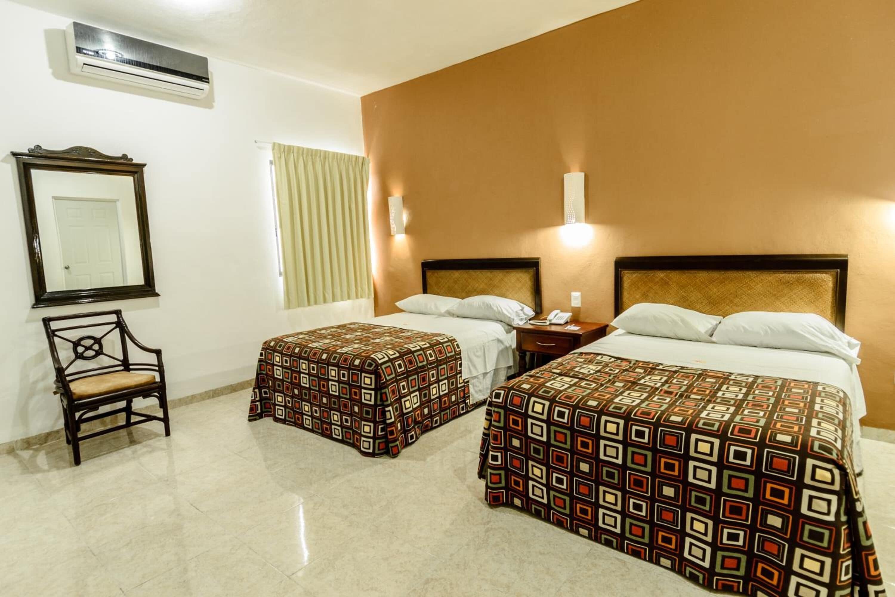 Habitación de hotel con dos camas, una silla y un espejo.