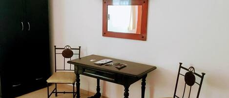 Um quarto com uma mesa de madeira escura, duas cadeiras, um guarda-roupa preto e uma televisão de tela plana fixada na parede.